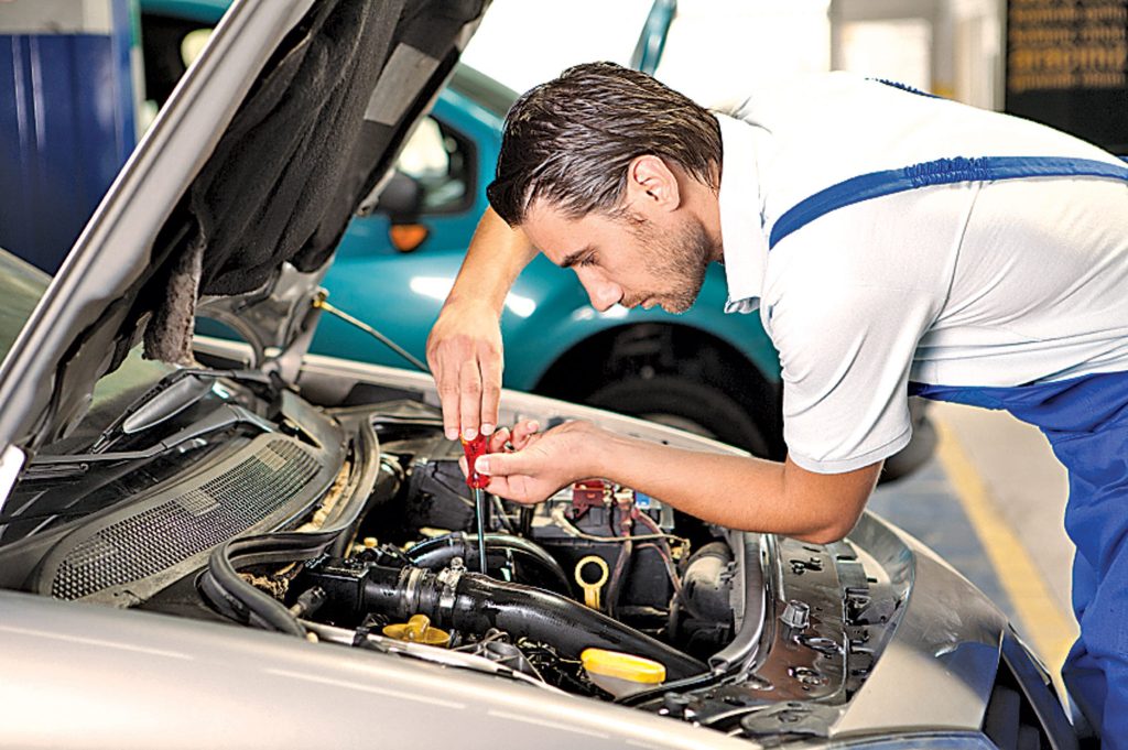 Mechanic referencing workshop manuals while repairing a car engine in a garage.