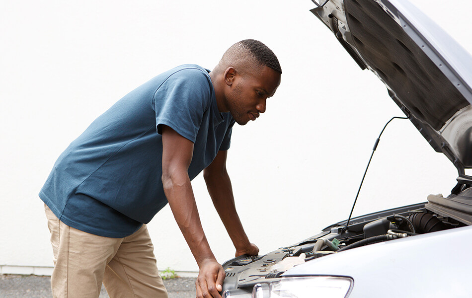 Man examining car engine, possibly using workshop manuals for reference.